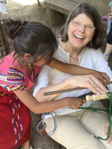A traveler is smiling and laughing, delighted to be learning how to backstrap weave as a Guatemalan weaver guides her hands on the loom.