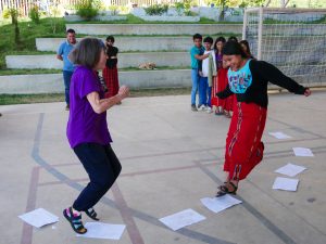 A traveler and a young Guatemalan school girl play a game hopping on paper on the floor.