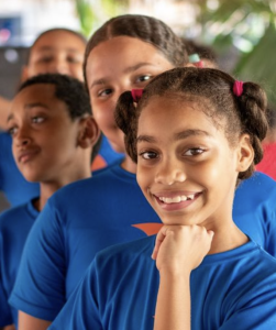 Children in blue shirts smile at the camera